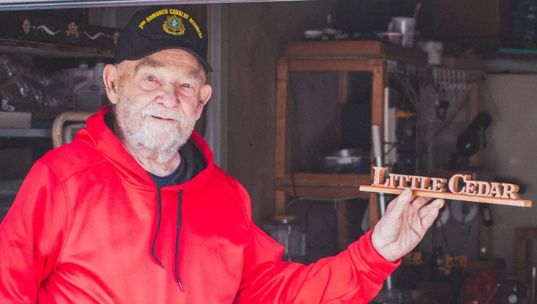 An older adult smiling while showing a wooden sign he crafted